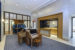 A hotel lobby with a reception desk, a seating area with a computer, and a large mirror. - Pentagon City Apartments near Pentagon Row - We Host (Arlington)