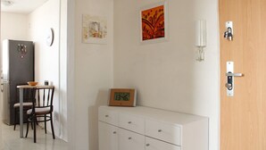 A kitchen with a refrigerator, a dining table with chairs, a clock, and a cabinet with a clock on top. - Small one room apartment with balcony (Humenné)