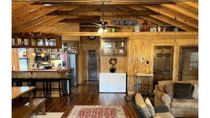 L’intérieur d’un chalet rustique est doté d’un plafond en bois, d’un coin repas avec des bancs, d’une cuisine équipée d’un réfrigérateur et d’un espace de vie avec un canapé et un tapis.