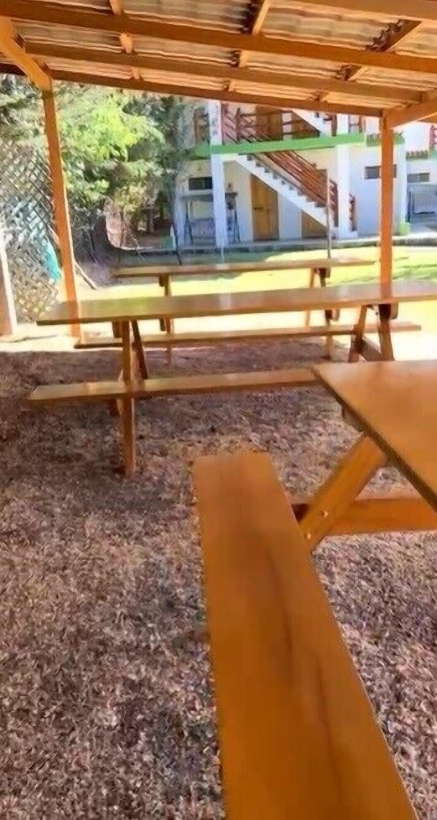Un espace extérieur abrité, équipé de tables de pique-nique et offrant une vue sur un bâtiment doté d’un escalier.