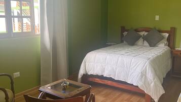Una habitación con cama, una mesa con bandeja, una silla y un ventanal con cortinas.