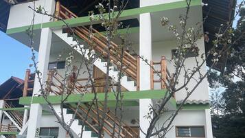 Un edificio de varios pisos con una escalera, un pequeño porche y un árbol en primer plano.
