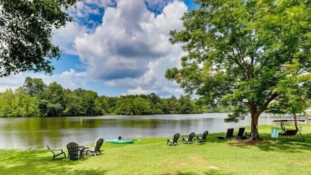 Un paisaje junto al lago con sillas, una mesa, un canoa y un árbol.