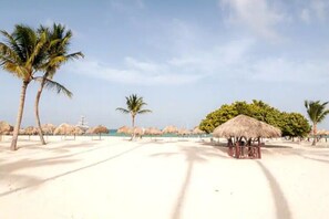 Une scène de plage avec des palmiers, une hutte à toit de chaume et un bâtiment situé au loin.
