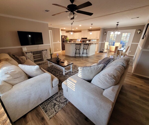 A spacious living room with a large gray sofa, a coffee table, and a TV. In the background, there is a kitchen with a bar area and a dining area. - Relax with your family or friends at this peaceful place to stay . (Navarre)
