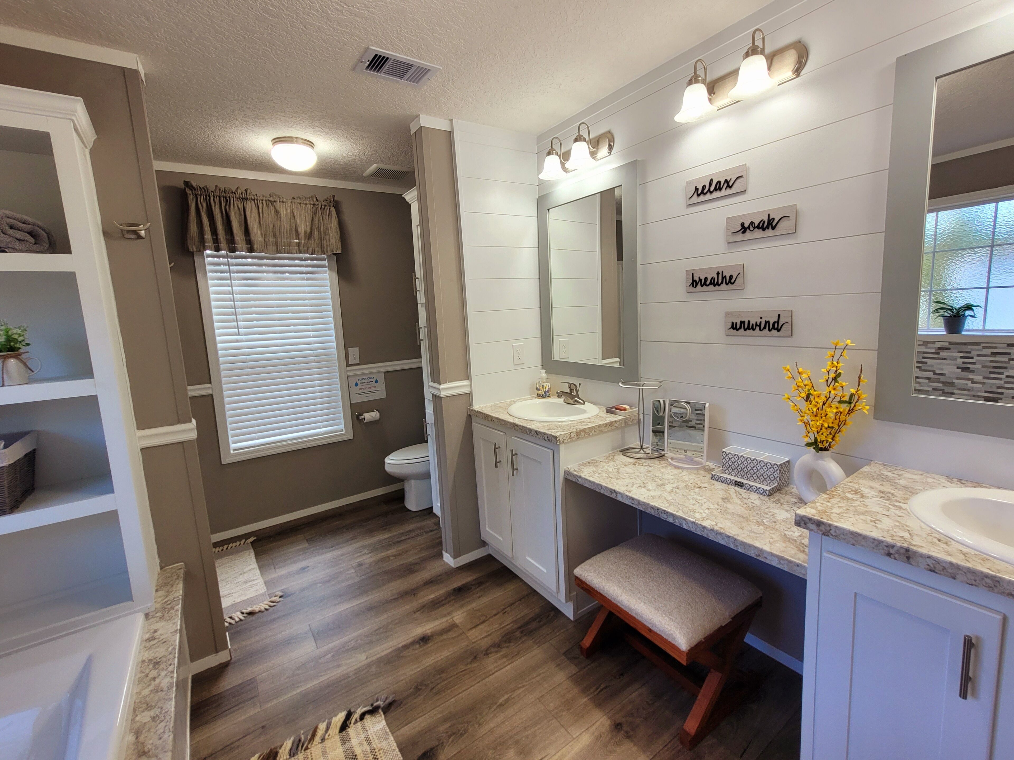 A modern bathroom with a vanity, sink, and mirror. There are decorative signs on the wall and a window with blinds.