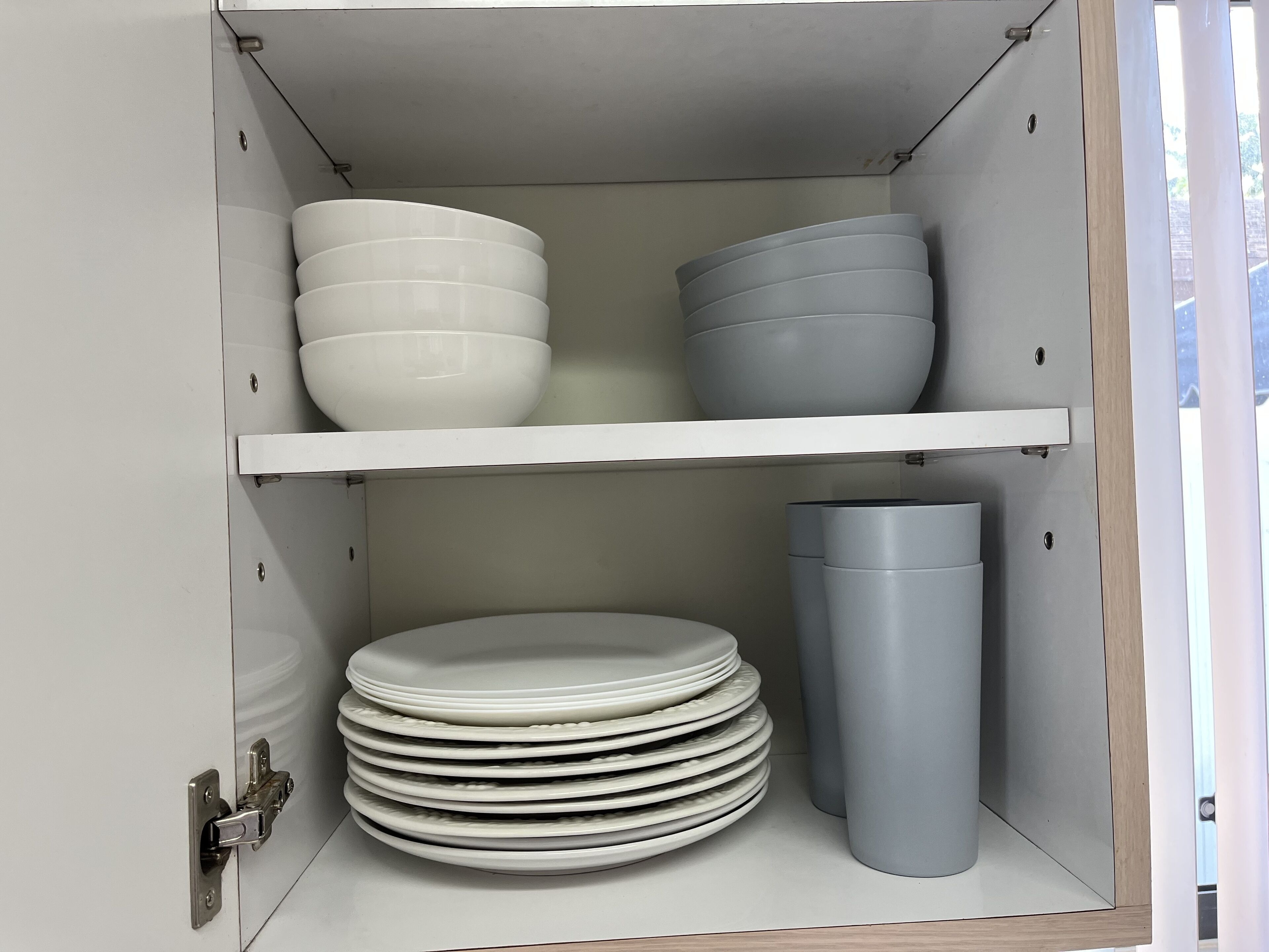 Un armario con repisas que contienen cuencos y platos blancos y grises, y un contenedor cilíndrico gris.