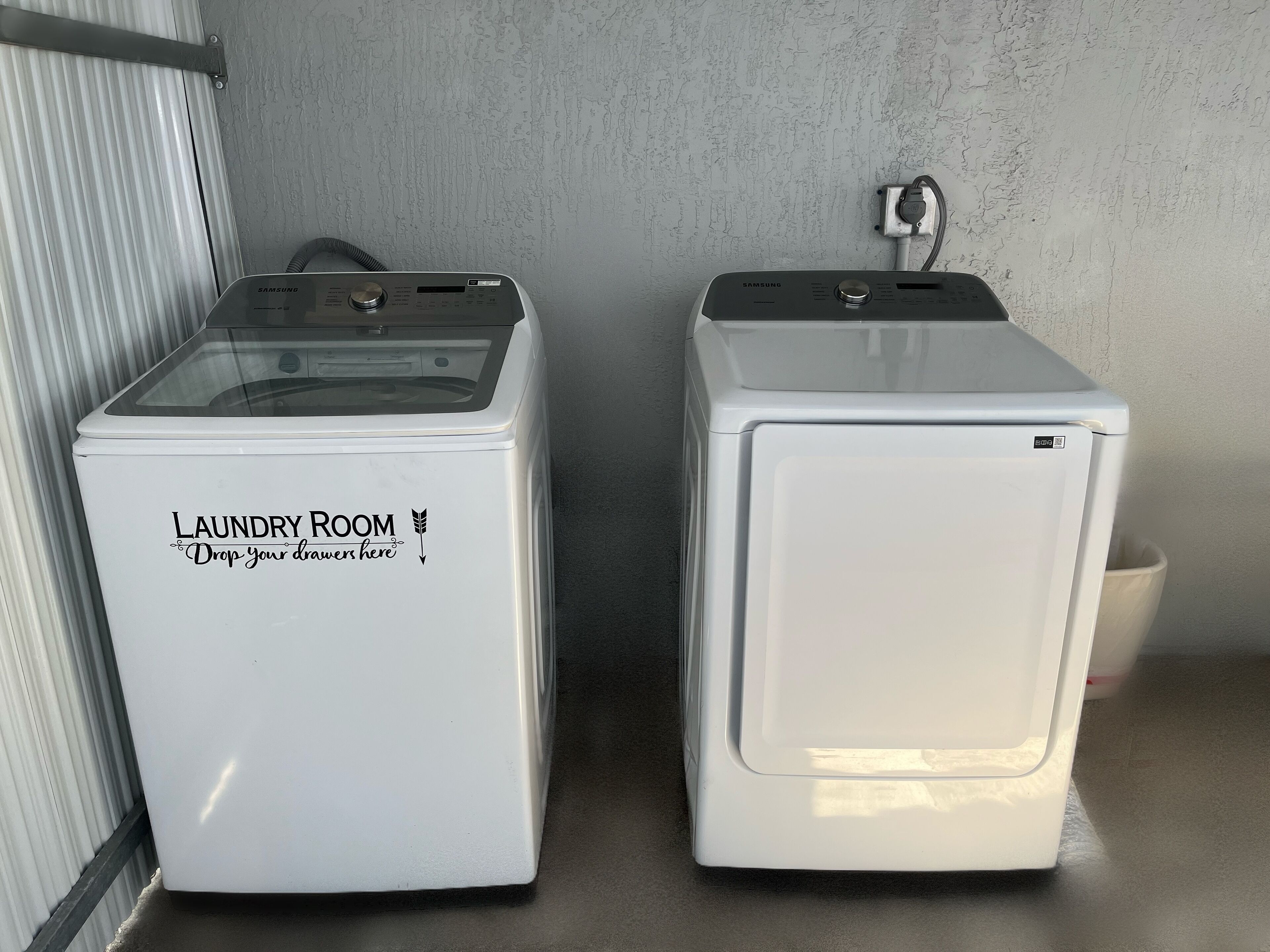 Two white laundry machines with a label that reads 'Laundry Room Drop your drawers here' on the left machine.