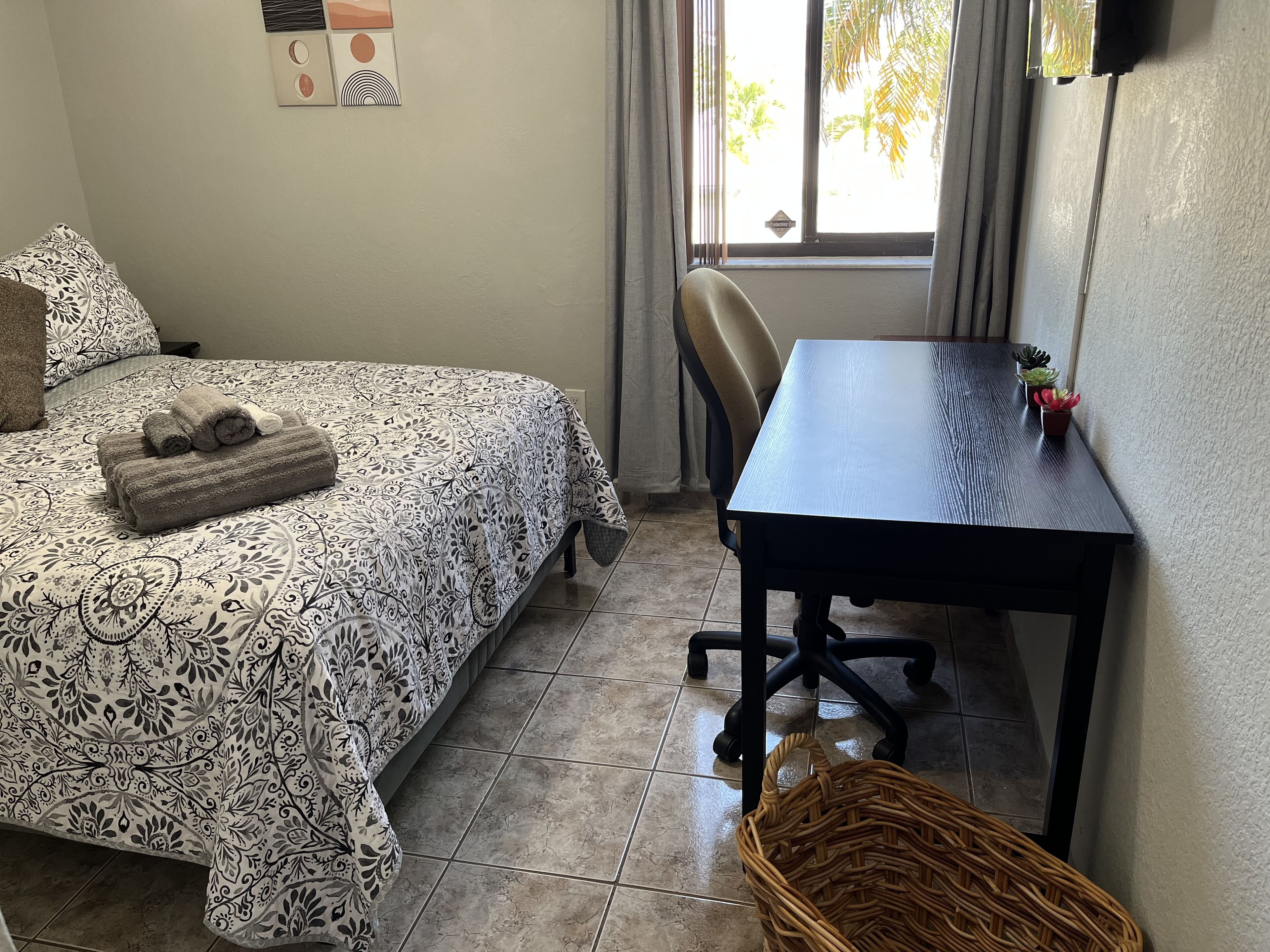 Une pièce comprenant un lit, un bureau, une chaise, une petite table avec des plantes et un panier en osier.