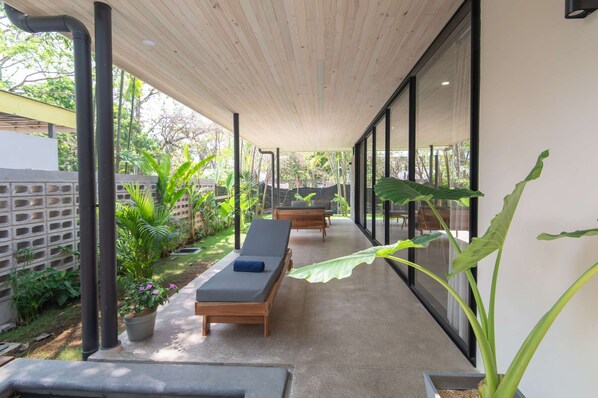 A covered outdoor area with two lounge chairs, a concrete floor, and potted plants.