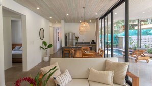 A modern living room with a sofa, dining table, and chairs, a kitchen area, and a view of an outdoor swimming pool. - Villa Arlen - Brand new - Pool - Spacious (Mal País de Cobano)