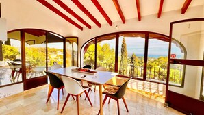 A dining area with a table and chairs, large windows with a view of trees and hills, and a ceiling with wooden beams. - VILLA CHRIS in Moraira – 4 bedrooms, private pool, panoramic sea and marina views, air conditioning and Wi-Fi (Moraira)