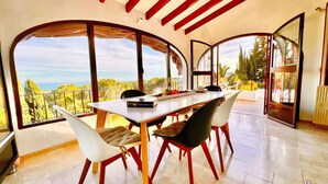A dining area with a table and chairs, large windows with a view of trees and the sky, and a red ceiling. - VILLA CHRIS in Moraira – 4 bedrooms, private pool, panoramic sea and marina views, air conditioning and Wi-Fi (Moraira)