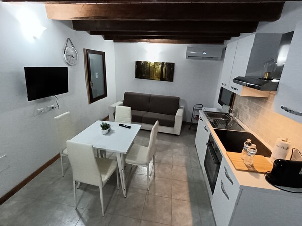 A compact living space with a dining area, a sofa, a TV, and a kitchenette. - Clare House (Apricale)