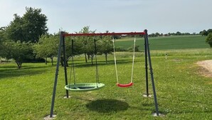 A swing set in a grassy field with trees in the background.