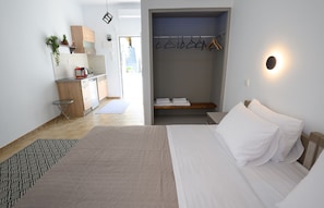 Une chambre avec un lit, une table de chevet, une petite table avec une bouilloire, un porte-vêtements et une vue sur l’extérieur.