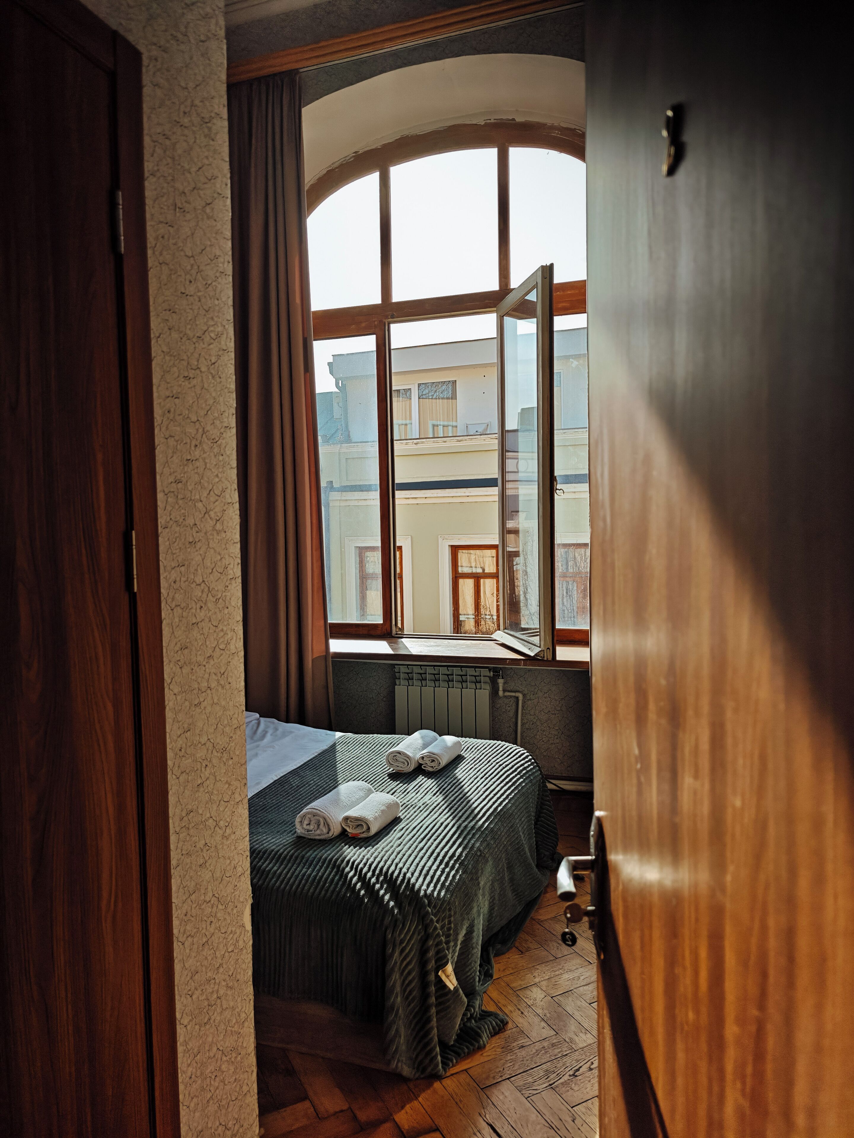 Ein Zimmer mit einem Bett, einem Fenster, einer Heizung und Blick auf Gebäude.