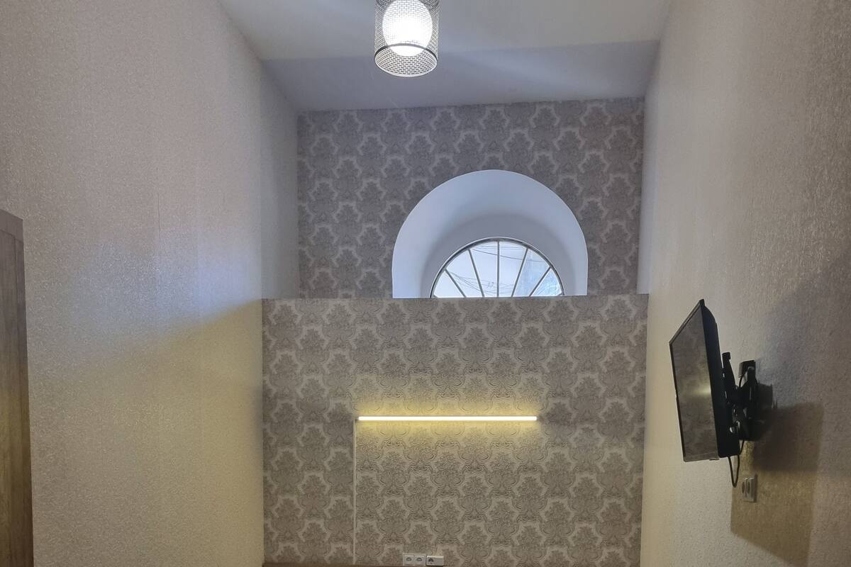 A small, dimly lit room with two beds, a wooden floor, a small window, and a wall-mounted TV.