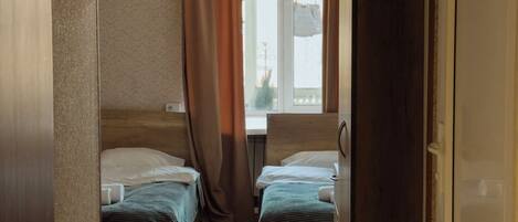 A room with two beds, a window with curtains, and a wooden floor.