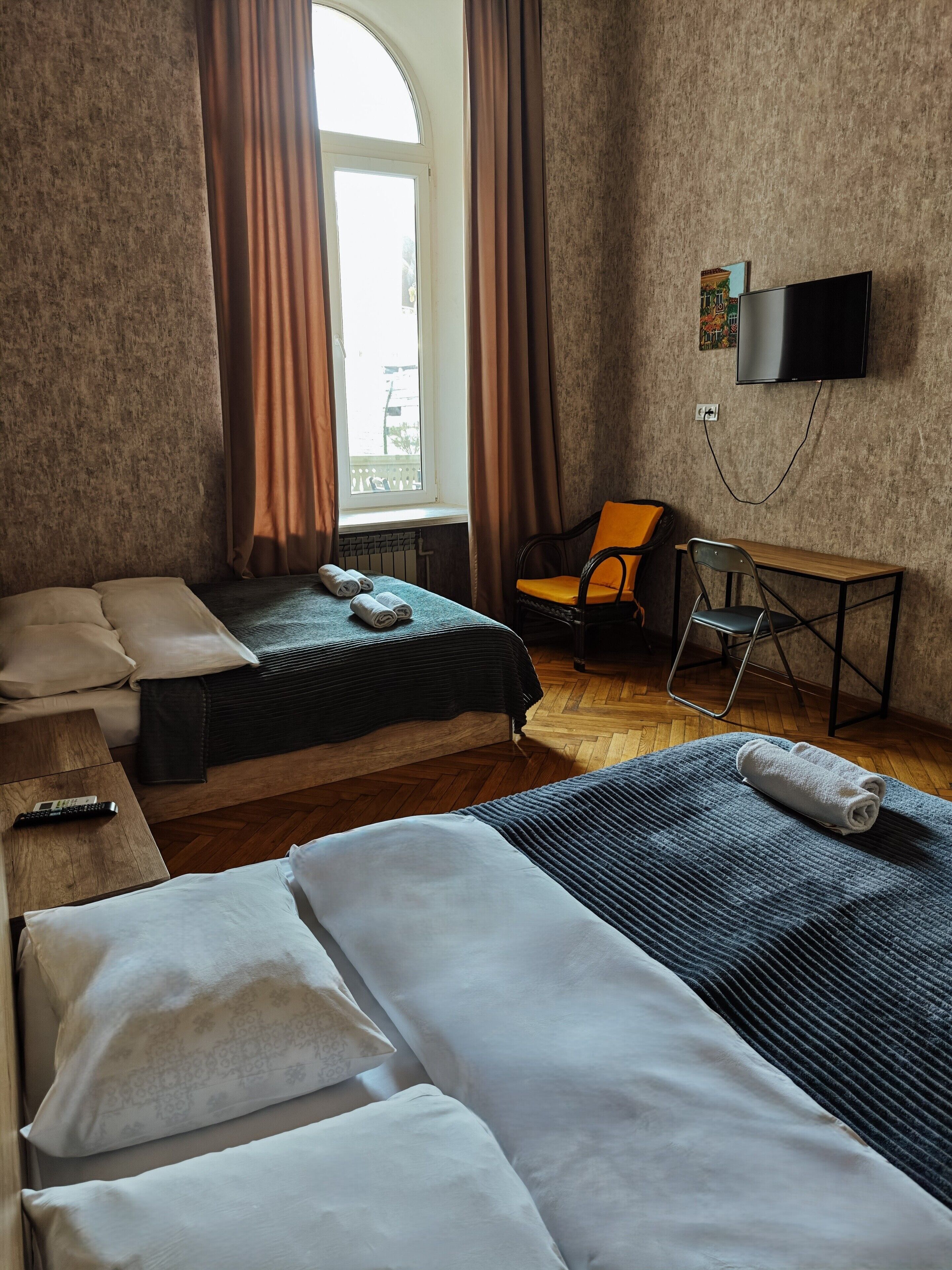 Habitación de hotel con dos camas, un escritorio, una silla, un televisor y una ventana con cortinas.