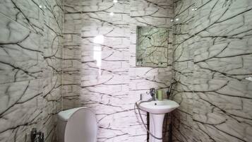 Un baño con paredes y suelo de mármol, un inodoro, un lavabo y un espejo.