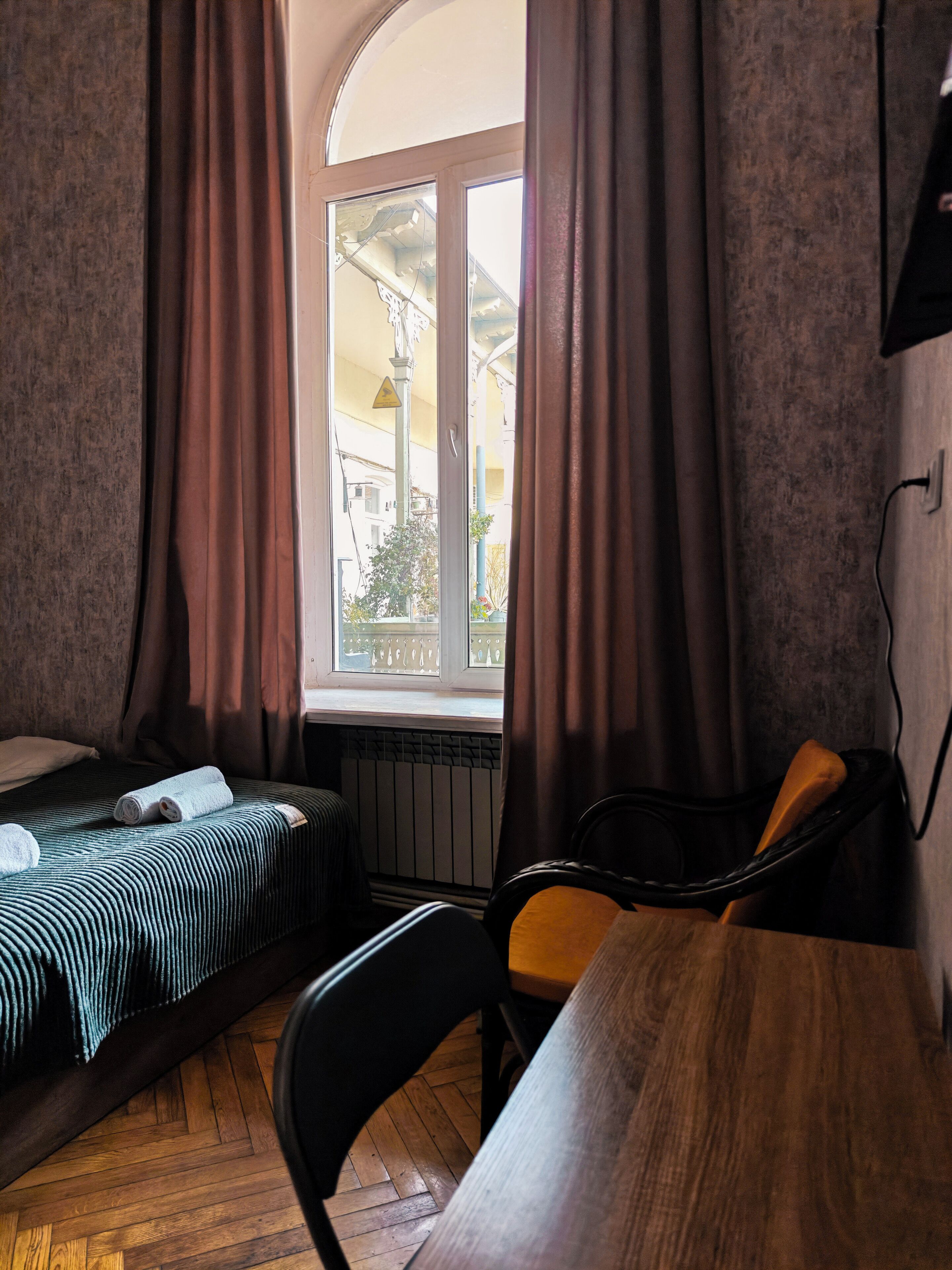 A small room with a bed, a wooden table, a chair, and a window with curtains.