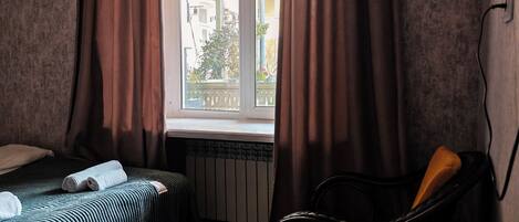 A small room with a bed, a wooden table, a chair, and a window with curtains.