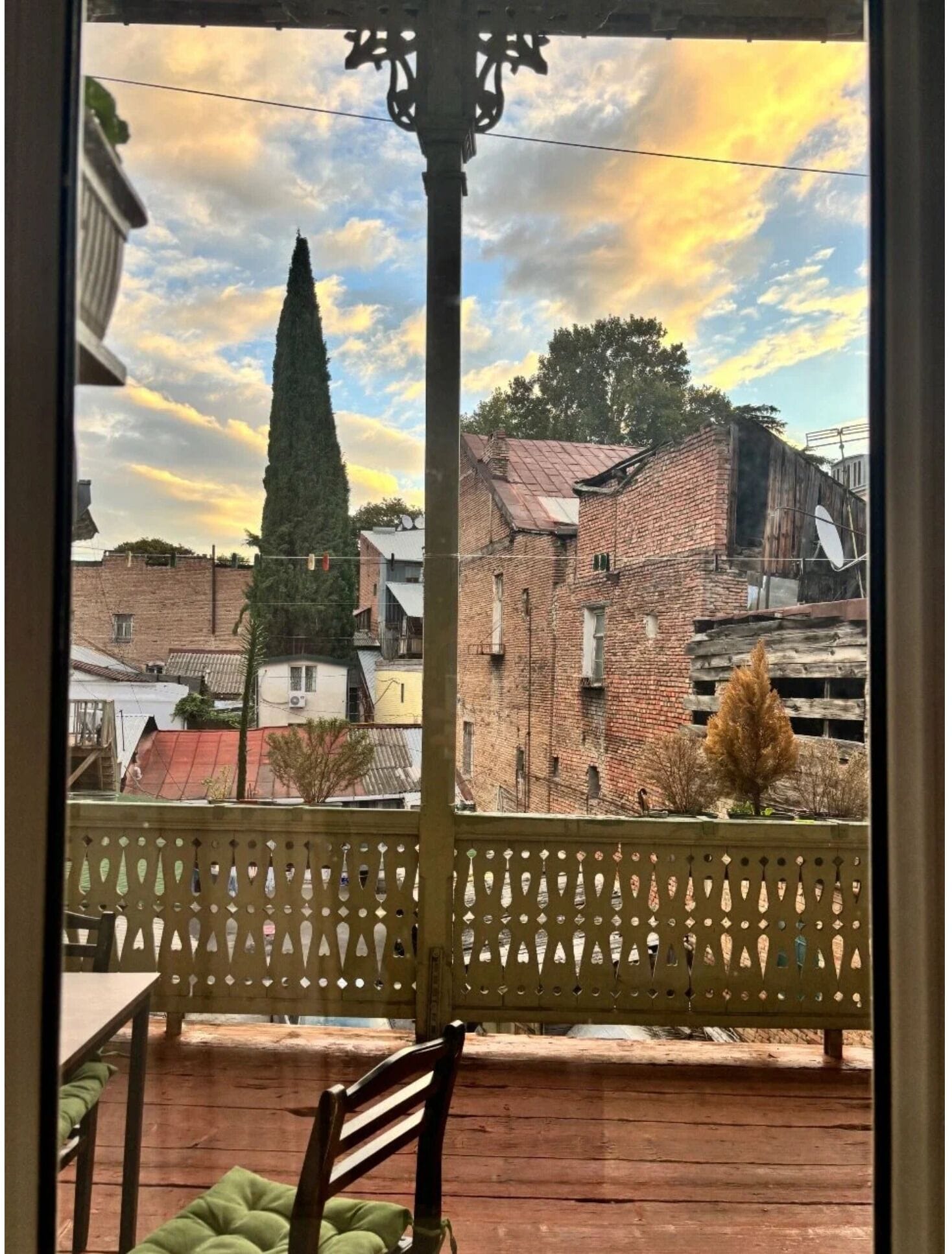 A balcony with a view of a town, featuring a tall church spire, brick buildings, and a wooden fence.
