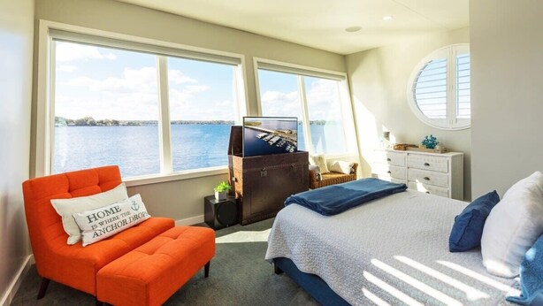 A bedroom with a large window, a bed, an orange chair, and a dresser. - New Floating Luxury: Unique Houseboat Retreat (Orange Park)