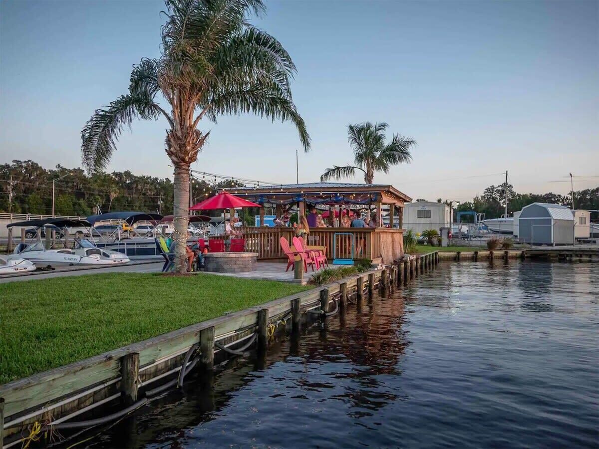 Un restaurant situé au bord de l’eau, avec une terrasse, un quai et des bateaux en arrière-plan.