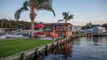 Un restaurant situé au bord de l’eau, avec une terrasse, un quai et des bateaux en arrière-plan.
