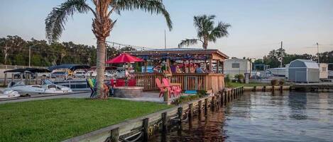 Un restaurante frente al agua con terraza, un muelle y barcos al fondo.