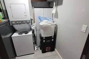 Een compacte keuken met een wasmachine, een kleine koelkast en een wasmand.