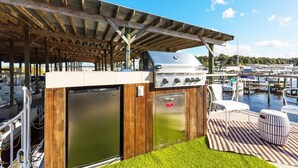 Een buitenkeuken met een barbecue, koelkast en zitplaatsen op een terras met uitzicht op een jachthaven.