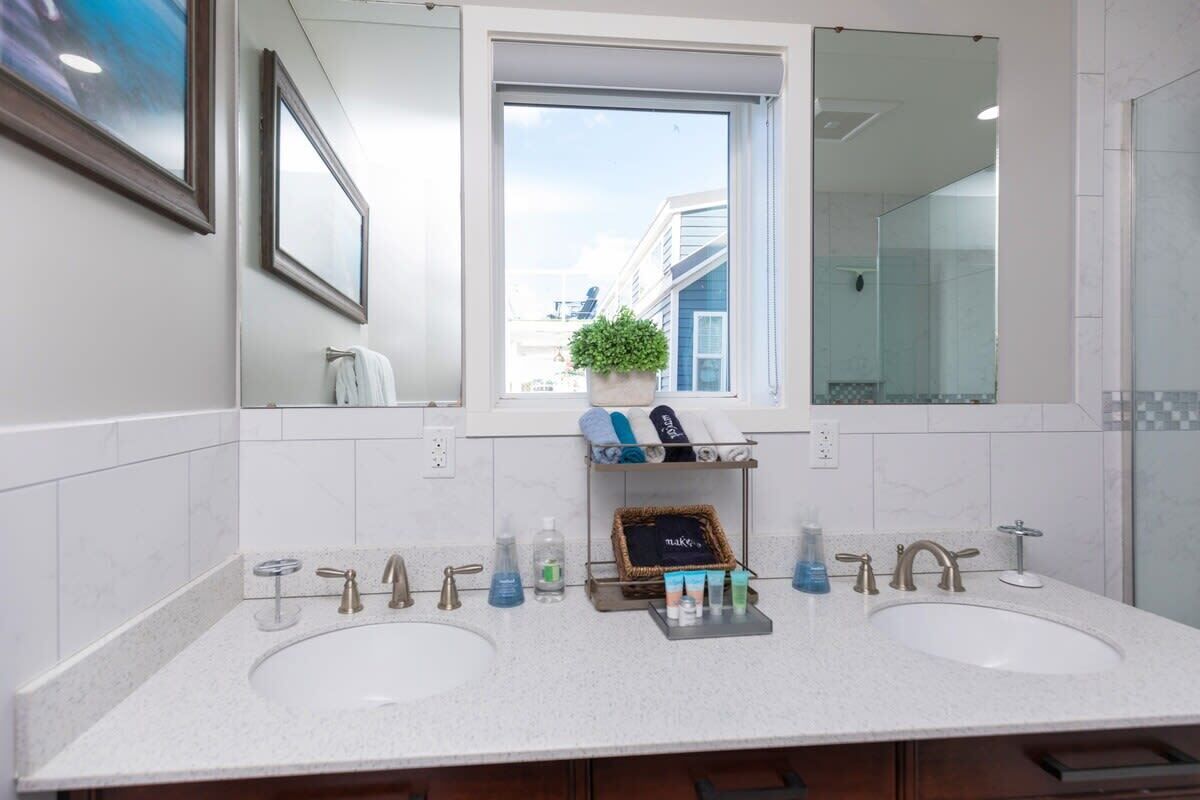 A modern bathroom with two sinks, a large mirror, and a window with a view of buildings.