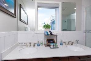 Une salle de bain moderne avec deux lavabos, un grand miroir et une fenêtre donnant sur des immeubles.
