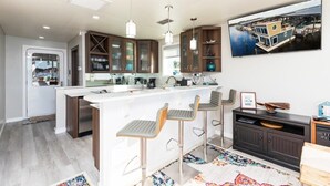 Een moderne keuken met een centraal eiland, barkrukken en een groot raam.
