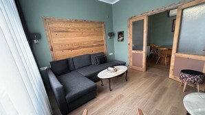 Ein gemütliches Wohnzimmer mit grauem Sofa, einem kleinen runden Tisch und einer Wand mit Holzverkleidung.