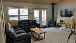 A cozy living room with a black leather sofa, a wooden coffee table, a TV, and a wood-burning stove. - Rio Cabin - Serenity on the South Fork (South Fork)