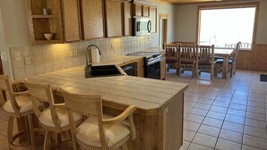 A kitchen with wooden cabinets, a built-in microwave, a sink, and a dining area with wooden chairs. - Rio Cabin - Serenity on the South Fork (South Fork)