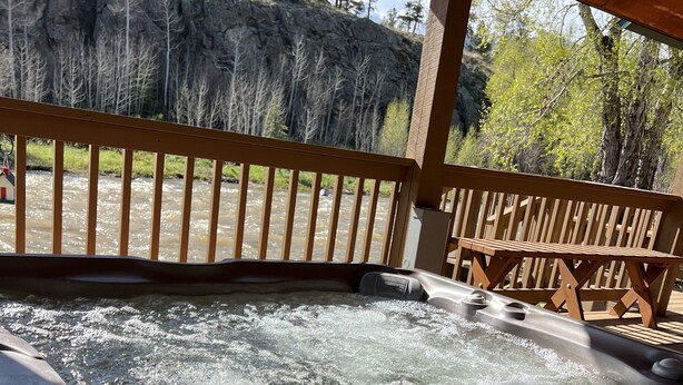 A hot tub with a wooden deck and a view of a river and forest. - Rio Cabin - Serenity on the South Fork (South Fork)
