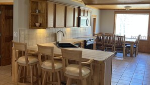 A kitchen with wooden cabinets, a tiled backsplash, a central island with stools, and a dining table with chairs. - Rio Cabin - Serenity on the South Fork (South Fork)