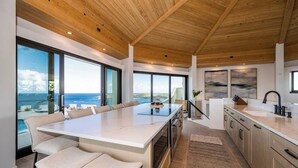 A modern kitchen with a large island, large windows, and a view of the ocean.