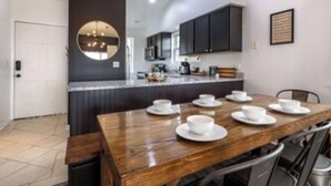 A modern kitchen with dark cabinets, a wooden dining table set with white plates and cups, and a large mirror on the wall. - Gated, Luxe Mid-Century Modern Condo| Walk to golf & pools! (Branson)
