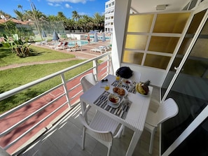Un balcón con mesa dispuesta para el desayuno, con vistas a una piscina con sillas de descanso y sombrillas.