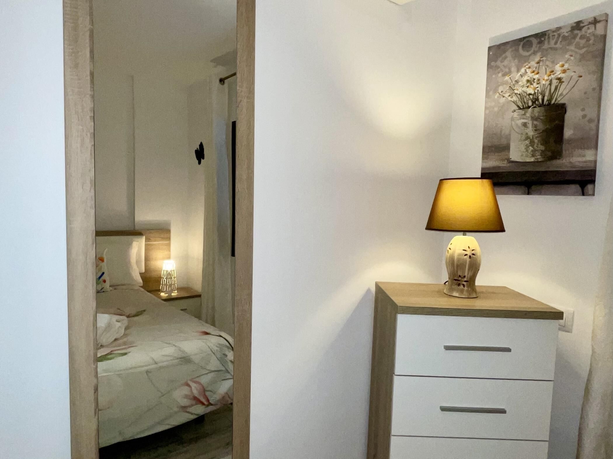 Et soveværelse med en seng, sengetæppe, lampe og et natbord.