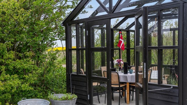 A glass greenhouse with a black frame, a table with chairs, and potted plants outside. - Stunning home in Vestervig with kitchen (Vestervig)