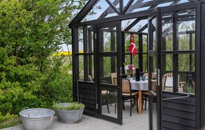 A glass greenhouse with a black frame, a table with chairs, and potted plants outside. - Stunning home in Vestervig with kitchen (Vestervig)