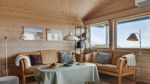 A cozy cabin interior with a wooden ceiling, a sofa, a table with a green tablecloth, and a bookshelf. - Stunning home in Vestervig with kitchen (Vestervig)