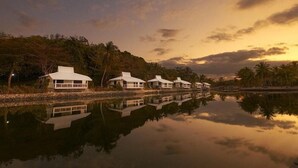 A row of white beach houses with a calm lake reflecting their structure, surrounded by lush greenery and palm trees. - Golden Sands Destination Resorts (Cebu Island)
